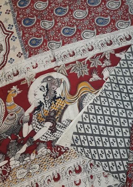 Maroon mul cotton kalamkari with a lady motif on pallu and wedding procession motif on border. The saree has paisley motif all over body.